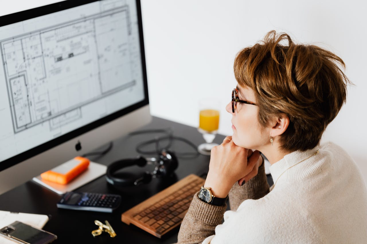 From above of concentrated adult female manager in eyeglasses analyzing data on computer while sitting at table in contemporary office
